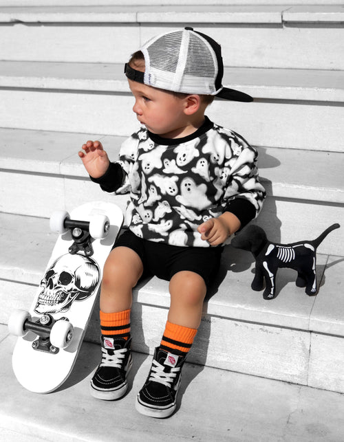 Child sitting on steps with a skateboard, wearing a black and white outfit with orange socks.
