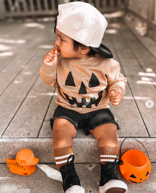 Toddler wearing a neutral pumpkin Halloween sweatshirt with jack-o-lantern face graphic, perfect for fall and Halloween outfits.
