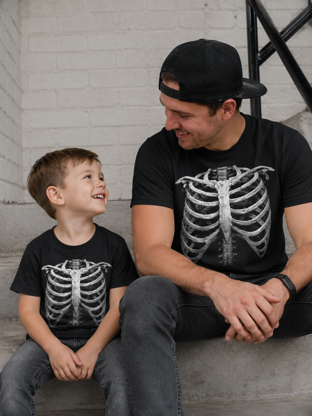 Man and child wearing black t-shirts with skeleton designs sitting on a staircase.